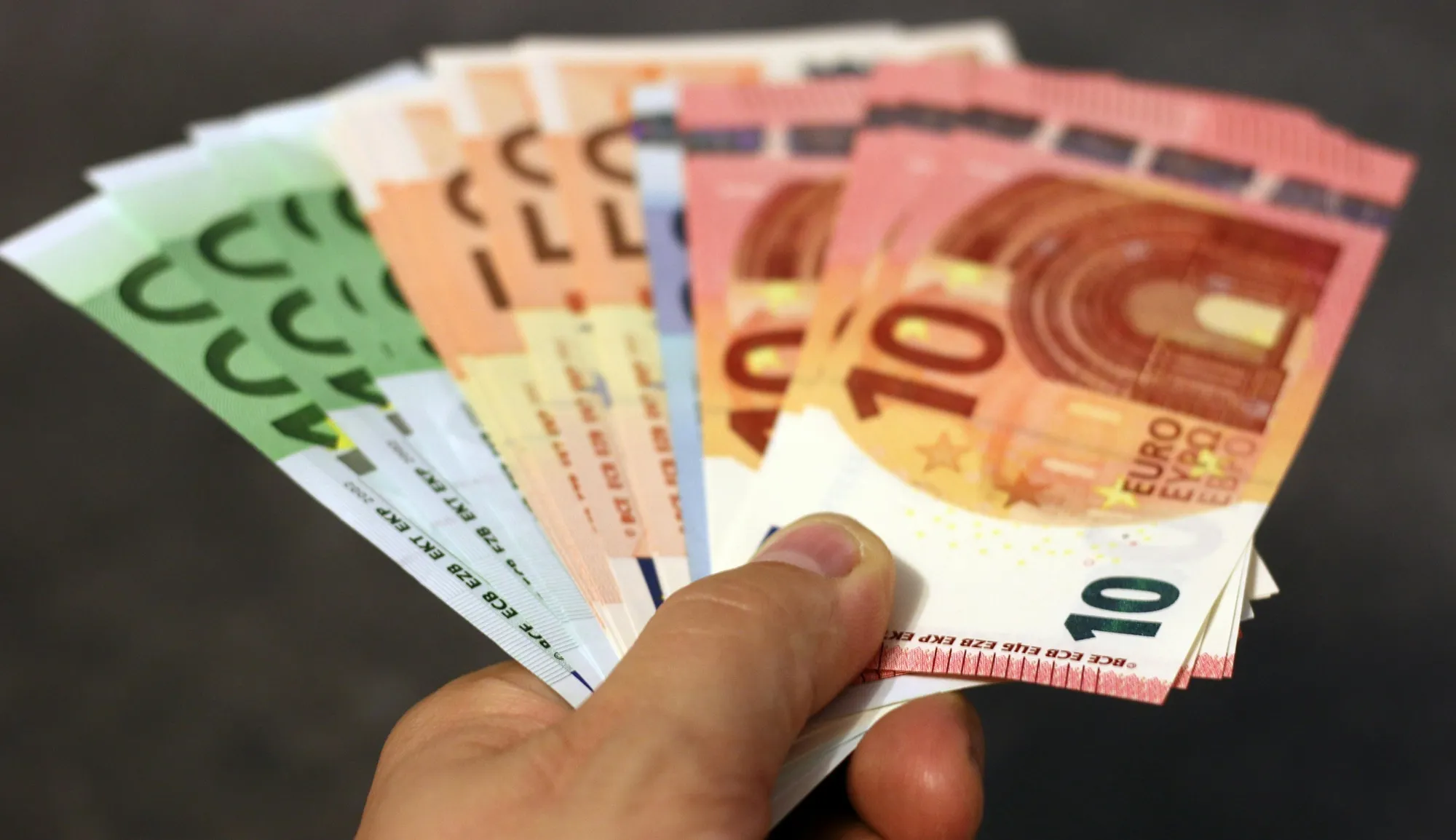 Ruka držiaca vejárovito rozložené eurobankovky rôznych nominálnych hodnôt, symbolizujúce rôzne úrovne cenových ponúk